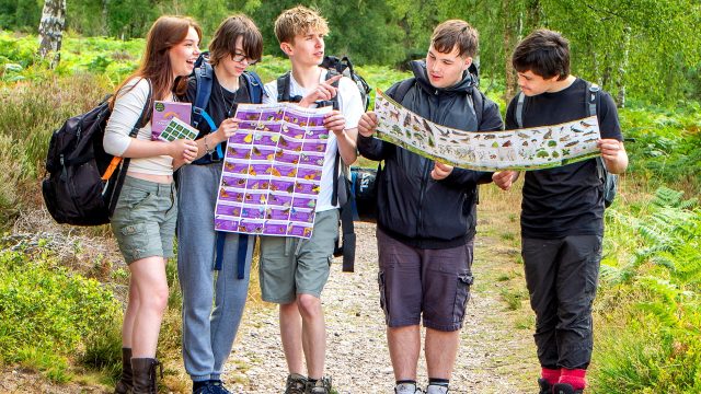 group of teenagers looking at wildlife guides in a wooded setting